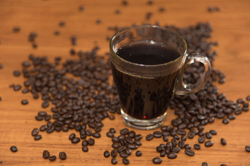 Black hot coffee on the teak wood table surrounding with coffee beans