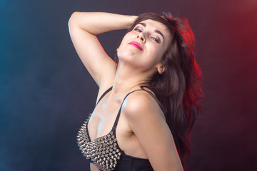 Naklejka premium Attractive young sexy brunette woman in riveted top posing in the studio on a dark background.