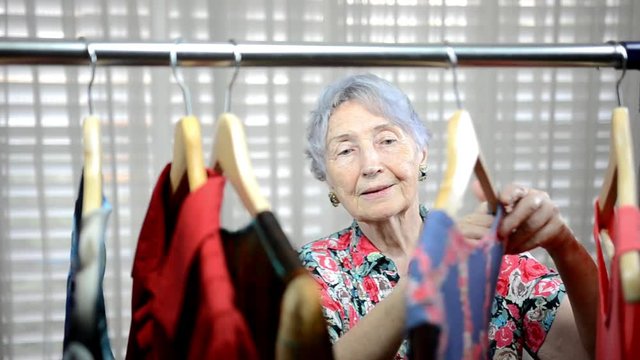Saleswoman taps a senior adult woman on the shoulder near clothing rack. Therefore she going away from the store.