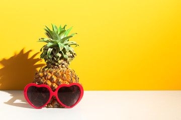 pineapple tropical fruit with fashion red heart sunglasses, hot summer season vacation holiday, yellow background, sunshine day, paradise travel tour and relax concept
