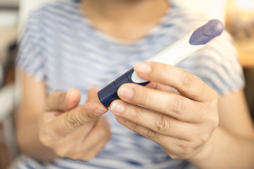 Close up of woman hands using lancet on finger to check blood sugar level by Glucose meter. Use as Medicine, diabetes, glycemia, health care and people concept.