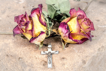 Christian cross on rosary and a dry yellow red roses lie on a sandstone