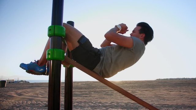 Hard workout of Hispanic guy exercising at beach training place at morning sunlight, powerful guy active lifestyle dressed in grey t-shirt and sportive outfit with white watches on strong hand