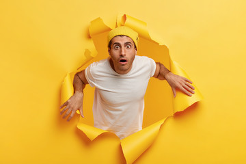 Indoor shot of puzzled shocked man looks in terror, being shocked by something, wears yellow hat...