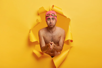 Topeless young male blows cheeks, keeps palms pressed together catches breath, prepares for diving...