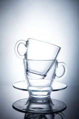 Two isolated transparent tea cups with saucers