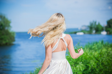 Fototapeta na wymiar Nice blonde lady at nature. Woman in flying silk white dress at outdoor, relax time 