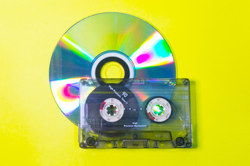 Compact disc and audio cassette on a yellow background.