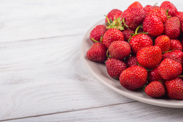 Strawberries on a plate on a white wooden background