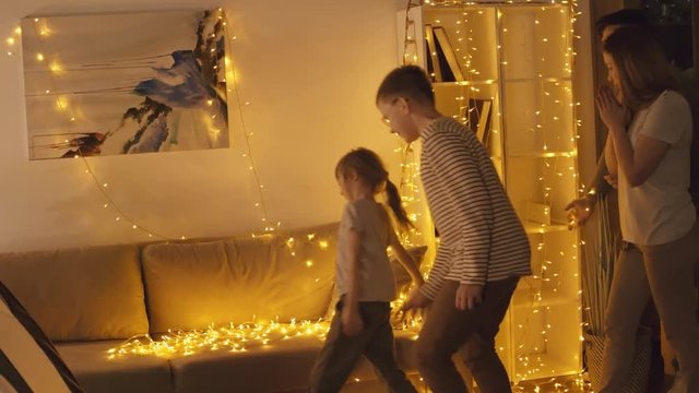 Medium shot of Caucasian parents and two kids turning on electric garland and decorating room with lights