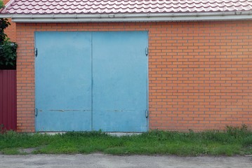 facade of a brown brick garage with blue metal gates in the street