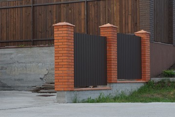 part of a brown metal fence and bricks on a gray road and green grass