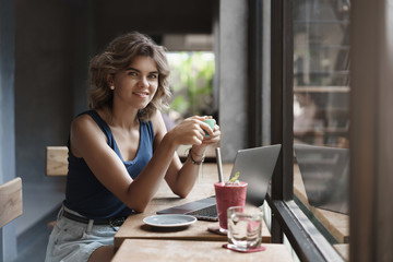 Charming european blond curly-haired female entrepreneur sit cafe window bar use laptop drinking coffee take break working freelance prepare university project, digital nomad concept