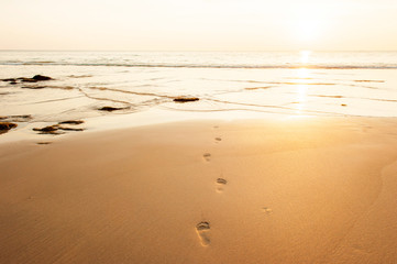 Bare footprints on the sand beach at sunset.