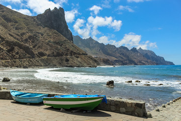 Fototapeta na wymiar Panoramic view of Aimasiga beach with volcanic black sand and lone rocks sticking out of the sea foam. Local fishing boats in the foreground. North coast of the island Tenerife, Spain