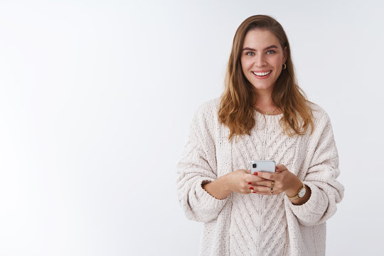 Studio shot charming happy smiling woman holding smartphone looking camera positive grinning communicating using app featurused. Female blogger posting pic online smm working via phone