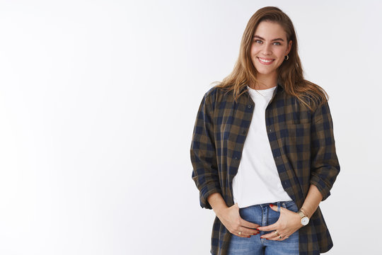 Feminine tender european girl giggling smiling broadly white teeth, wearing casual checked shirt holding hands pockets self-assured, body-positive and carefree, standing white background
