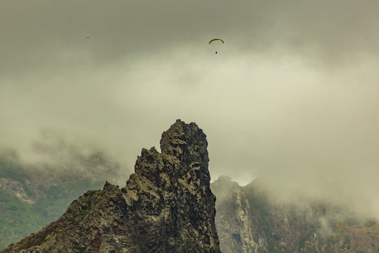 Lonly paraglider between low dense clouds and mountain peak near village of Garachico, Tenerife, Spain - Powered by Adobe