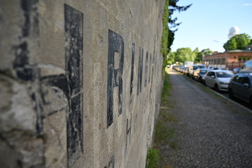 Fototapeta premium Black letters on the wall of a cemetery in Berlin-Germany. Parked cars in a street nearby a cemetery.