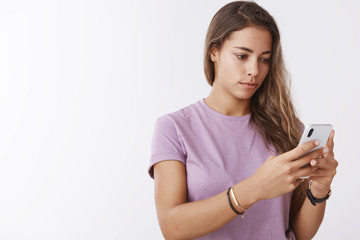 Fototapeta premium Serious-looking focused young woman holding smartphone looking display edditing selfie using photo app, thinking what write social media blog, messaging, searching cellular signal