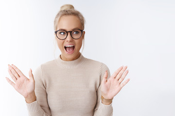 Excited attractive blond woman in glasses screaming amazed and thrilled emotive over awesome news...