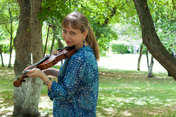 The young Russian woman with a violin costs at a tree in the park in the summer