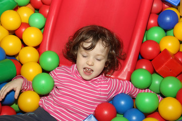 Fototapeta na wymiar Little curly cute smile girl plays in balls for a dry pool. Play room. Happiness.