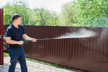 Gun water hose nozzle sprayer. A man's hand holds a black gun watering hose with splash. Man...