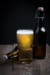 glass of lager beer and a bottle on a dark background