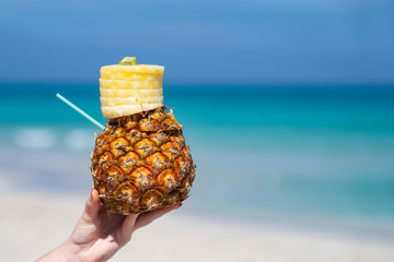 Woman hand holds tropical pineapple cocktail on the beach. Beautiful sea ocean sky white sand beach. Cuba space for text