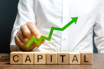 A businessman is holding a green up arrow above the word Capital. Increasing the attractiveness of...