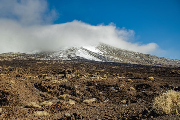 Mountain Teide with white snow spots, partly covered by the clouds. Bright blue sky. Teide National Park, Tenerife, Canary Islands, Spain.