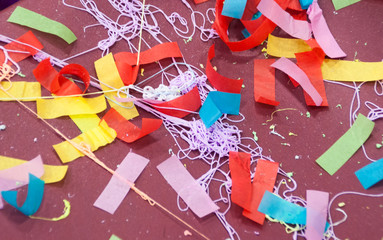 Red, yellow, pink, green, and blue streamers, confetti, and string on a maroon background