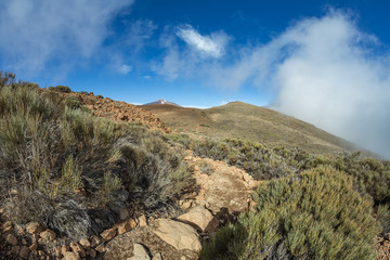 Mountains around volcano Teide, partly covered by the clouds. Bright blue sky. Teide National Park, Tenerife, Canary Islands, Spain.