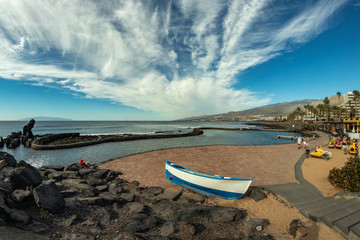 Coastline in Las Americas, Tenerife, Spain. Bright lue sky with beautiful clouds. Fishing boat in the foreground. La Gomera Island view.