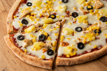 Pizza topped with sauce, chicken, cheese and pineapple serve on wooden plate on wooden table. Photo of Hawaiian pizza. 