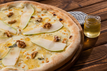 Traditional pizza with pear, nuts and blue cheese on a wooden background. Close up. Top view.