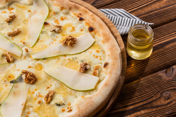 Traditional pizza with pear, nuts and blue cheese on a wooden background. Close up. Top view.