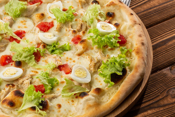 Delicious pizza Caesar style with white sauce, chicken, parmesan, egg, cherry tomatoes and fresh lettuce at wooden background. Restaurant pizzeria menu with delicious taste pizza Caesar 