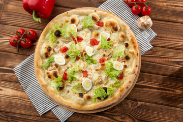 Delicious pizza Caesar style with white sauce, chicken, parmesan, egg, cherry tomatoes and fresh lettuce at wooden background. Restaurant pizzeria menu with delicious taste pizza Caesar 