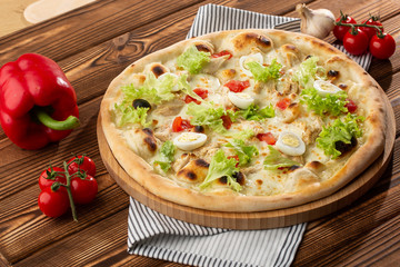 Delicious pizza Caesar style with white sauce, chicken, parmesan, egg, cherry tomatoes and fresh lettuce at wooden background. Restaurant pizzeria menu with delicious taste pizza Caesar 