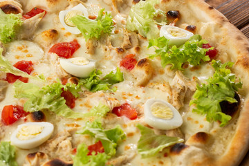 Delicious pizza Caesar style with white sauce, chicken, parmesan, egg, cherry tomatoes and fresh lettuce at wooden background. Restaurant pizzeria menu with delicious taste pizza Caesar 