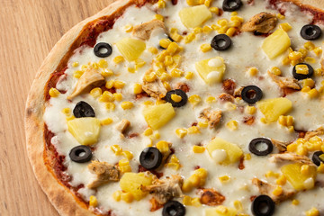 Pizza topped with sauce, chicken, cheese and pineapple serve on wooden plate on wooden table. Photo of Hawaiian pizza. 