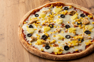 Pizza topped with sauce, chicken, cheese and pineapple serve on wooden plate on wooden table. Photo of Hawaiian pizza. 