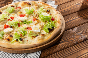 Delicious pizza Caesar style with white sauce, chicken, parmesan, egg, cherry tomatoes and fresh lettuce at wooden background. Restaurant pizzeria menu with delicious taste pizza Caesar 