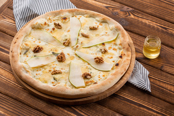 Traditional pizza with pear, nuts and blue cheese on a wooden background. Close up. Top view.