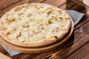 Pizza topped with sauce, chicken, cheese and pineapple serve on wooden plate on wooden table. Photo of Hawaiian pizza. 