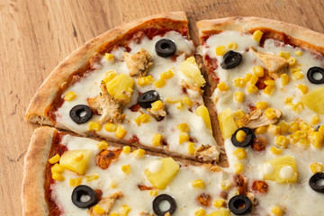 Pizza topped with sauce, chicken, cheese and pineapple serve on wooden plate on wooden table. Photo of Hawaiian pizza. 