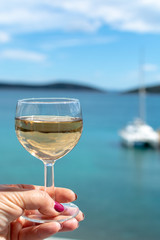 hand with glass of white wine served outside on balcony with sea view