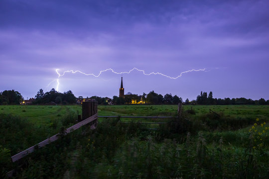 Lightning storm strikes near a small village at in in farmland